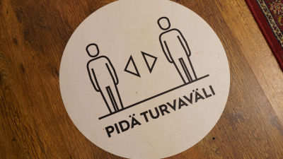 Ett klistermärke på ett golv som påminner om att man ska hålla säkerhetsavstånd.