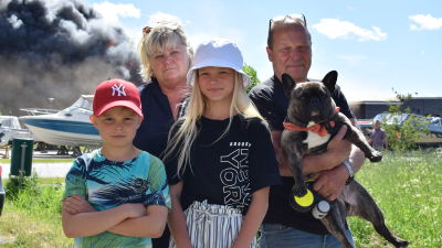 En familj på fyra personer och en hund står med det brinnande varuhuset Hurrikaani i bakgrunden.
