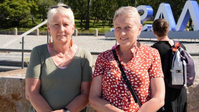 Två korthåriga och leende kvinnor står nära varandra.