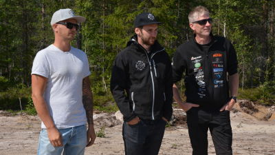 Tre män står och tittar på en motocross.