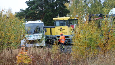 Ett lok har kört in i en buss. Bussen ligger tvärsöver rälsen med loket in i vänstra sidan.