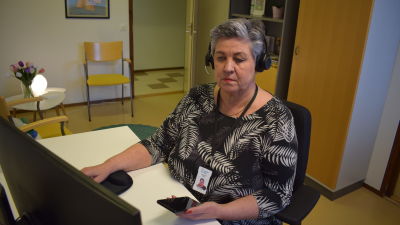 Hanne Brown, en dam med grått hår, sitter med hörlurar på vid en dator och jobbar i ett kontorsrum.