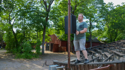 En man står uppe på kanten till en läktare och hänger upp en högtalare.