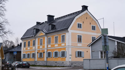 Ett gult trävåningshus med julljusstakar i fönstrena.