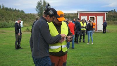 Två män tittar på en telefon. I bakgrunden syns en kö med människor.
