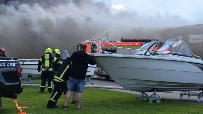 Räddningverket och privatpersoner tömmer båtar från en brinnande byggnad.