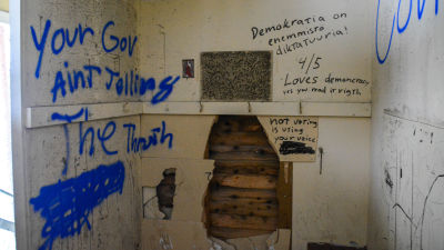 Ett litet rum som vandaliserats. Text på väggarna. Ett stort hål i en av väggarna.