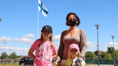 En kvinna med två barn. I bakgrunden svajar Finlands flagga.