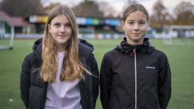 Alina Johansson och Emelie Enberg står utomhus på en konstgräsplan och tittar in i kameran.