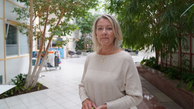 Mona Burlin ser in i kameran. I bakgrunden en korridor med växter.