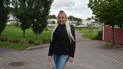 Bild på Satu Söderström, kommunfullmäktigeledamot, som står framför två träd.