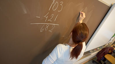 En grundskolelärare skriver på en svart tavla