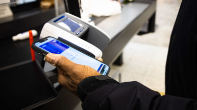 Henkilö maksaa mobiilisti ostokset ruokakaupassa.