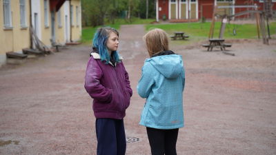 Två skolbarn som står på skolgården och talar