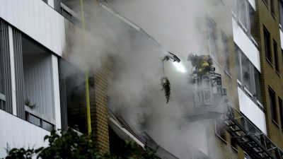 Brandman i skylift spanar in i ett brinnande hus.