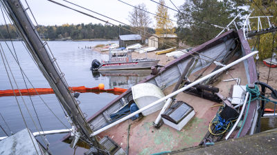En sjunkande trålare ligger förtöjd vid en kaj. I bakgrunden syns en räddningsbåt och oljabommar som avgränsar området kring trålaren.