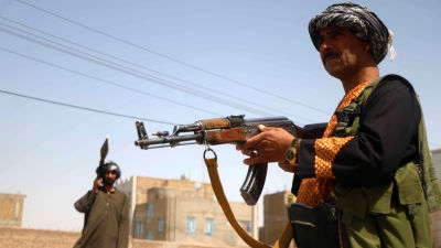 Två beväpnade afghanska milismän. I bakgrunden syns en mur och ett hus.