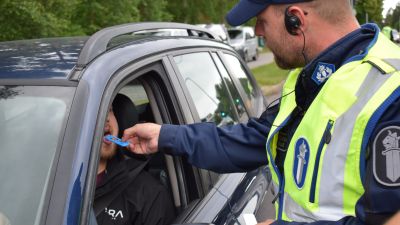 Polis utför ett blårstest för bilist som sitter i sin blåa bil.