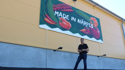 En man står intill en gul vägg. På väggen finns en stor skylt med texten Made in Närpes.