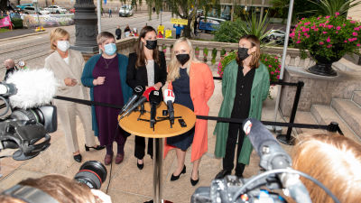 Partiledarna i Sanna Marins regering står bakom ett runt bord fyllt med mikrofoner och fotograferas.