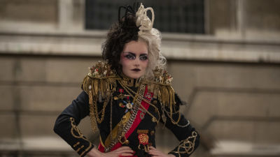 Cruella (Emma Stone) i bestämd med händerna i sidorna iklädd en punk/armé-inspirerad rock.