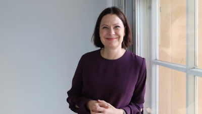 Minna Arve vid ett fönster. Hon ser rakt i kameran.
