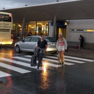 En buss står utanför Vasa flygplats. Två personer med resväskor går över vägen. Det är blött på marken.