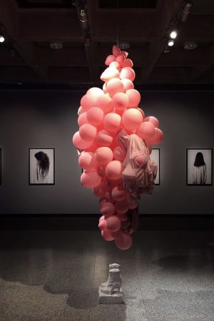 Installationen Intimately Social 4.09 här visad i utställningen Between No Bodies på Ålands Konstmuseum 2018. I bakgrunden Nayab Ikrams fotoserie In Between. Foto på rosa ballongkluster