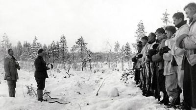 Soldater under vinterkriget står uppställda på led med huvudbonaderna i händerna.