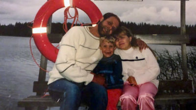 Anette, hennes lillebror och hennes pappa sitter på en bänk vid stranden. Det är sommarkväll och de kramas och ler mot kameran.