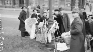 Här samlas barn år 1943 på en gata i Helsingfors för att köpa majviskor. Barn som samlats på gatan runt en person som säljer majviskor.