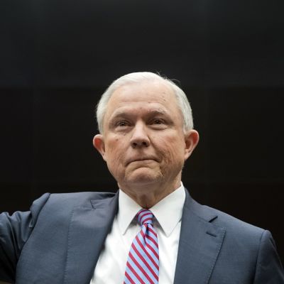 Jeff Sessions mustaa taustaa vasten kuvattuna. Sessionsilla on yllään tummanharmaa puku. Hän pitää oikeaa kättään ylhäällä vannoessaan todistajanvalaa.