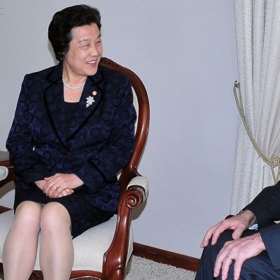 Wu ja Santos istuvat tuoleilla vaaleassa huoneessa ja keskustelevat. Wu hymyilee