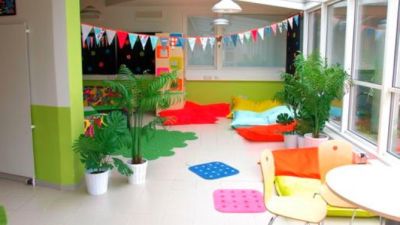 Ett ljust rum med glada färger, ljust golv med mattor, dynor och gröna växter.