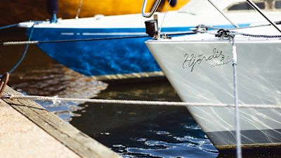 Två segelbåtar står förtöjda i en brygga. Den ena båten har ingraverat namnet "Hjördis" i fören.