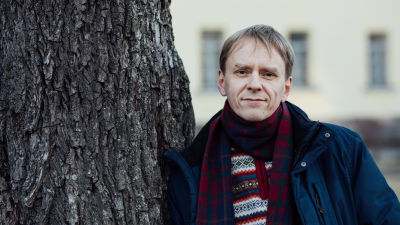 En ljushårig man lutar sig mot en trädstam.