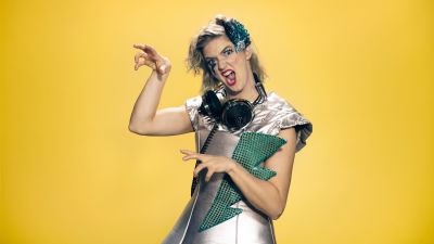 Programledaren Lisa Gerkman i Lady Gaga inspirerad outfit poserar med händerna som klor. Gul bakgrund.