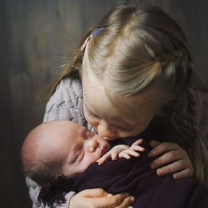 Syskonpar en liten flicka och en baby kramas.