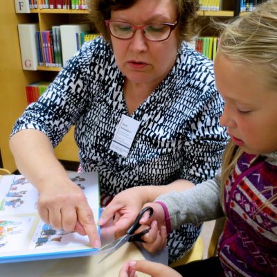 Silmälasipäinen nainen auttaa kontaktimuovin leikkamisessa nuorta tyttöä