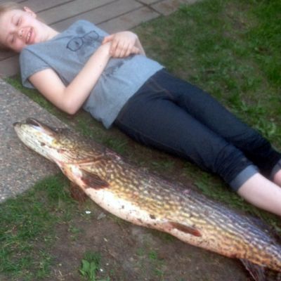 Tyttö makaa nurmikolla vieressä pitkä ja iso hauki
