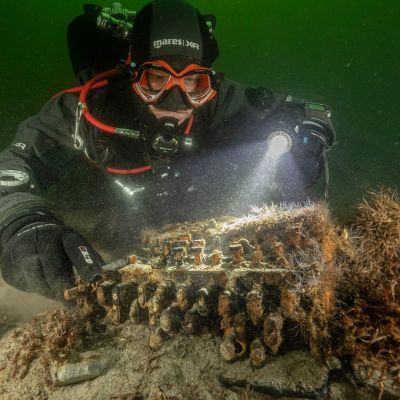 Sukeltaja valaisee lampulla verkkoa ja siihen takertunutta ruosteista laitetta.