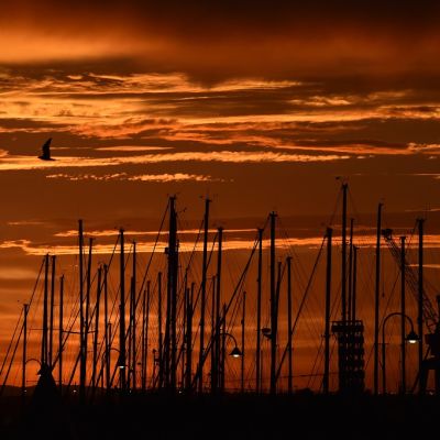 Oranssinpunainen auringonnousu veneiden mastojen takana.