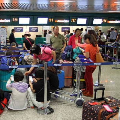 Matkustajat odottavat lentokentällä matkaan pääsyä ja istuvat lattialla.