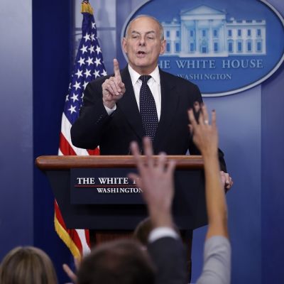 Kuvassa Valkoisen talon kansliapäällikkö John Kelly on puhumassa toimittajille. Etualalla viittaavia käsiä.