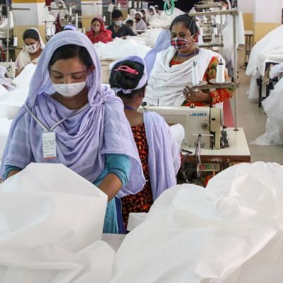 Kuvassa tekstiilitehtaan työntekijöitä Bangladeshin pääkaupungissa Dhakassa. Etualalla naistyöntekijä ja valkoista kangasta.