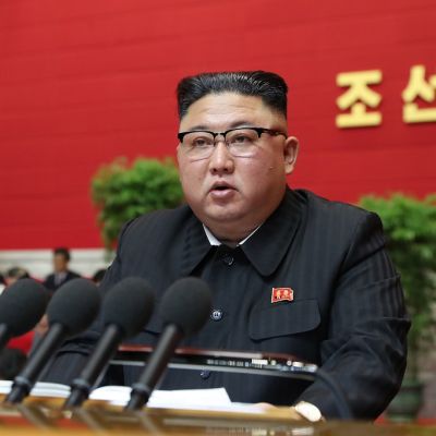 Kim Jong-un istuu pöydän takana. Hänen edessään on useita mikrofoneja.