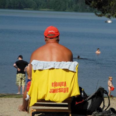 Rantavahti istuu Tuomiojärven rannallta, ihmisiä uimassa.