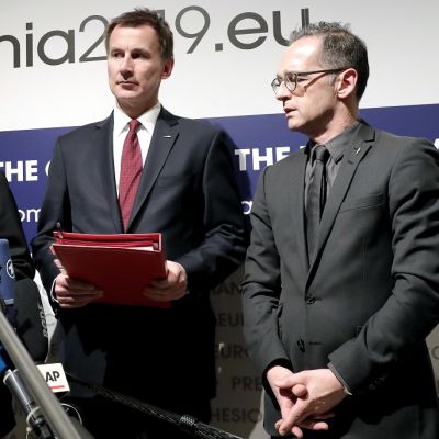 Ministerit pitävät tiedotustilaisuutta. Ranskan ulkoministeri puhuu mikrofonirykelmälle. Britannian ulkoministerillä on kädessään punainen kansio.