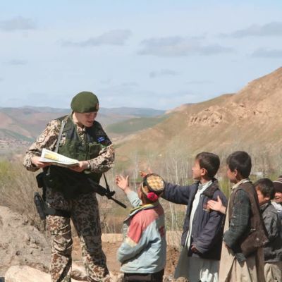 Elli Flen i uniform i Afghanistan, omgiven av barn med utsträckta händer.