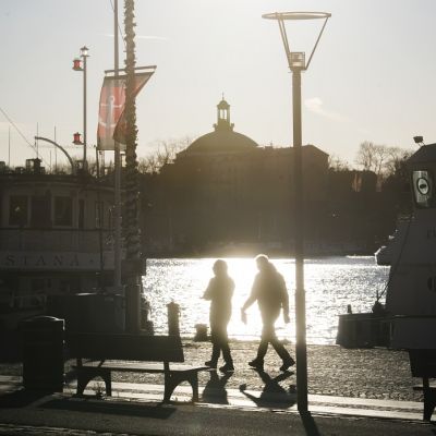 Kaupungin siluetti, tummia hahmoja etualalla.
